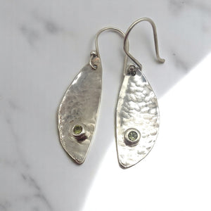 Handcrafted sterling silver earrings made from vintage spoon bowls, featuring a hammered texture and bezel-set green peridot stones, with hand-forged sterling silver hooks.